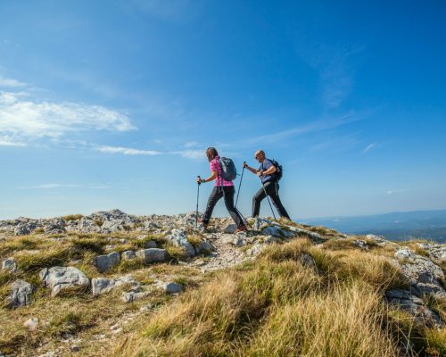 A couple hiking on Nanos Plateau in Slovenia against a blue sky